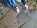Applying clear tape to the edge of an
        aluminum foil panel for the Modified CooKit solar cooker.