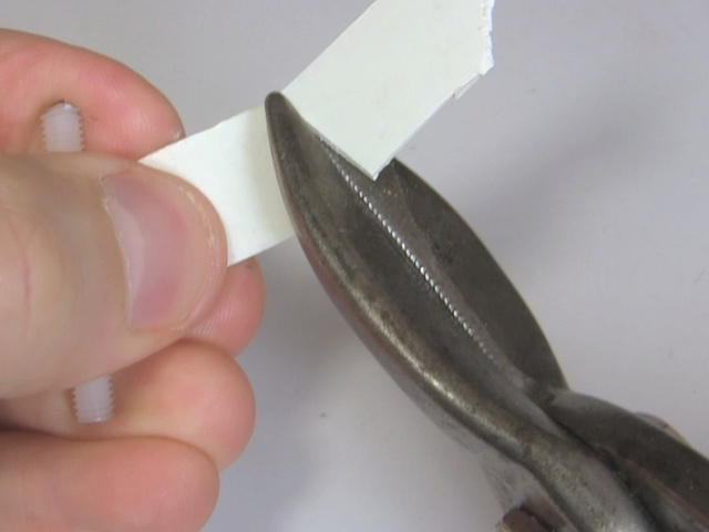 Using tin snips to cut a piece of plastic into a wedge shape.