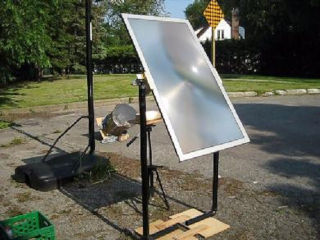 A large fresnel lense mounted in a stand outdoors facing the sun and focused with a bright spot on a brick.