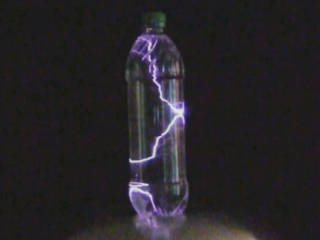 Photo of a plastic bottle filled with water sitting on a Van de Graaff generator with arcs, lightning, filling its interior.