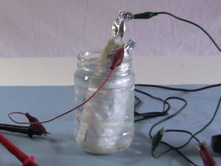 A DIY electrolitic capacitor with wires attached and being formed.