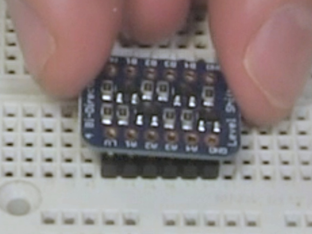 Placing the board on the pins while they sit in the breadboard.